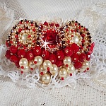Broche Rubis brod&eacute;e avec trois cabochons Ivoire et Rouge &agrave; laquelle s&rsquo;ajoute des toupies aux couleurs Cristal, Burgundy et Garnet, des perles nacr&eacute;es et opaque. Mont&eacute; sur une dentelle et une broche